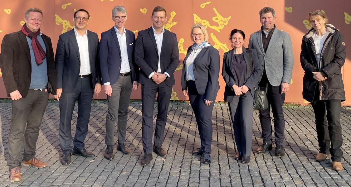 Gruppenfoto vor der Außenwand des BSL-4-Labors, auf der das Marburg Virus schematisch dargestellt ist
