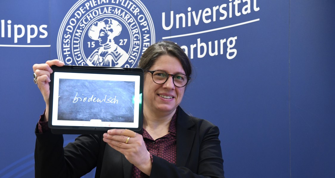 Prof. Dr. Constanze Spieß von der Philipps-Universität Marburg zeigt auf einem Tablet das Unwort des Jahres 2024.