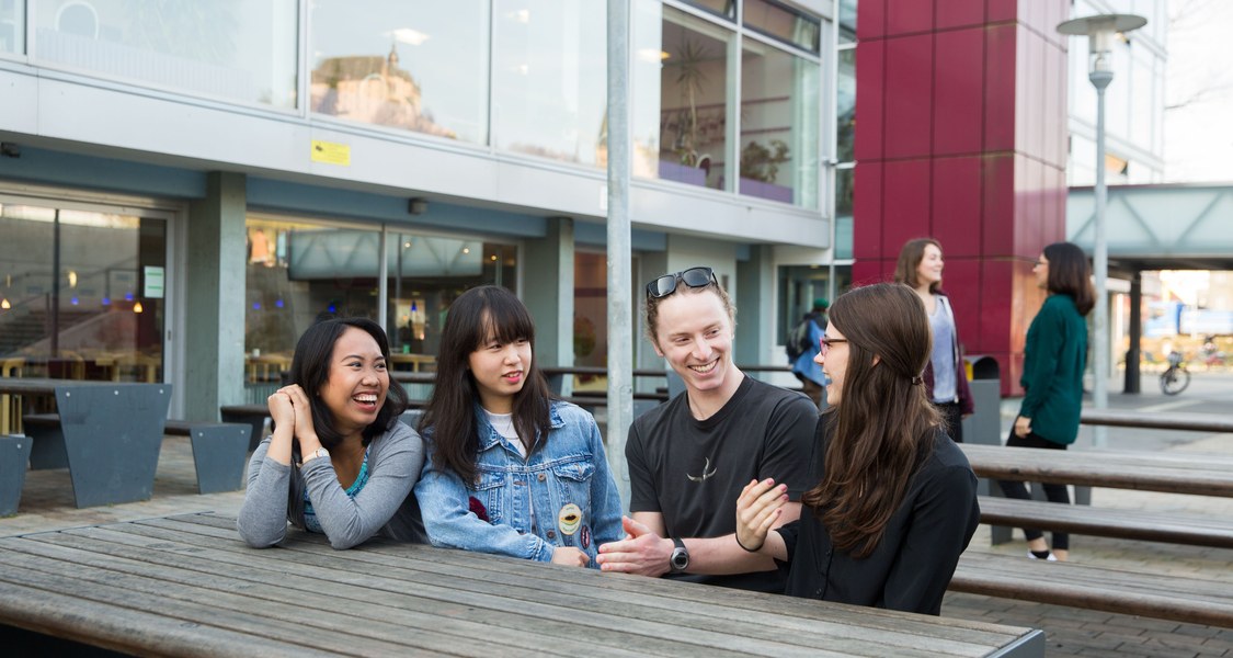 Studierende sitzen bei den Mensatischen draußen