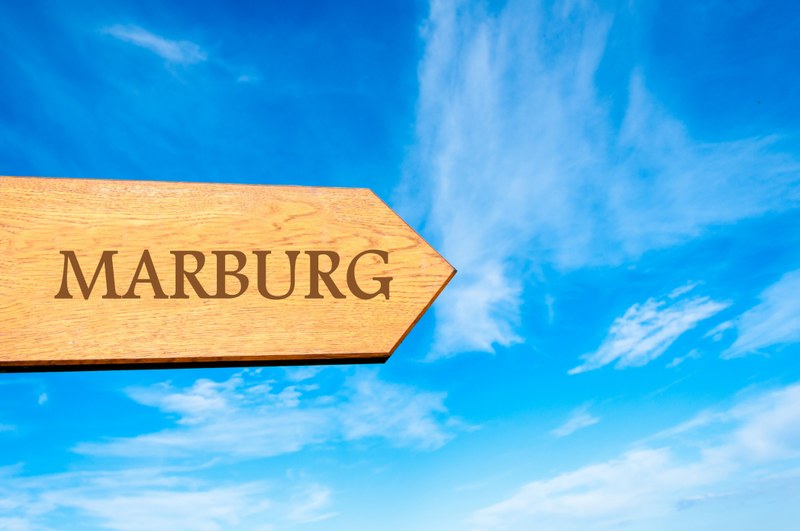 Hölzernes Schild , das die Aufschrift "Marburg" trägt und vor blauem Himmel die Richtung anzeigt.