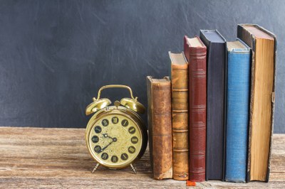 Neben einem alten Wecker stehend einige Bücher auf einem Tisch.