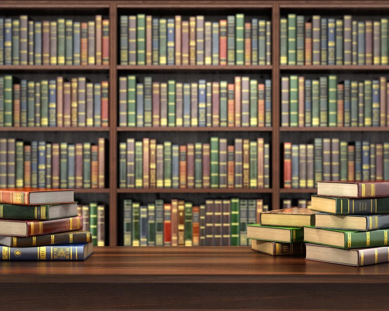 Ein Tisch mit Bücherstapeln vor einer Bücherregalwand