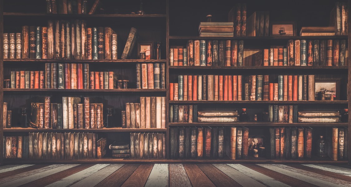 Ein langes mit alten Büchern gefülltes Regal vor einem Holzbretterboden.