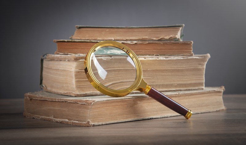 An einem Stapel liegender alter Bücher lehnte eine Lupe.