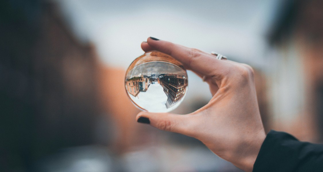 A hand holding a glass ball that shows an inverted reflection of a city.