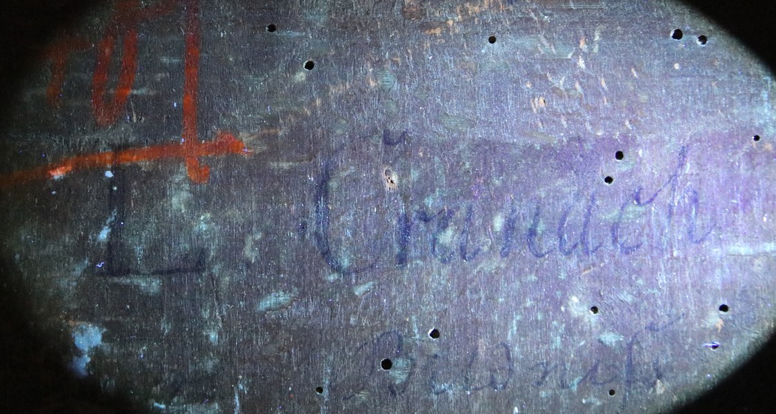 In einem hell erleuchteten, bläulich schimmernden Oval ist die Rückseite eines Gemäldes mit verschiedenen Markierungen und Wurmspuren erkennbar sowie dem Schriftzug "L. Cranach"