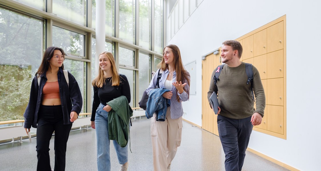 Studierende gehen nebeneinander durchs Foyer des Deutschen Sprachatlas und unterhalten sich miteinander