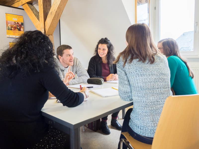 Eine Gruppe Studierender diskutiert lebhaft an einem Tisch.