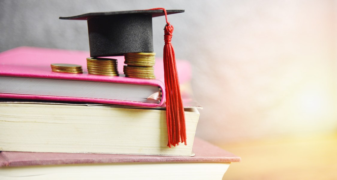 Bücher, Münzen und ein Studierendenhut.