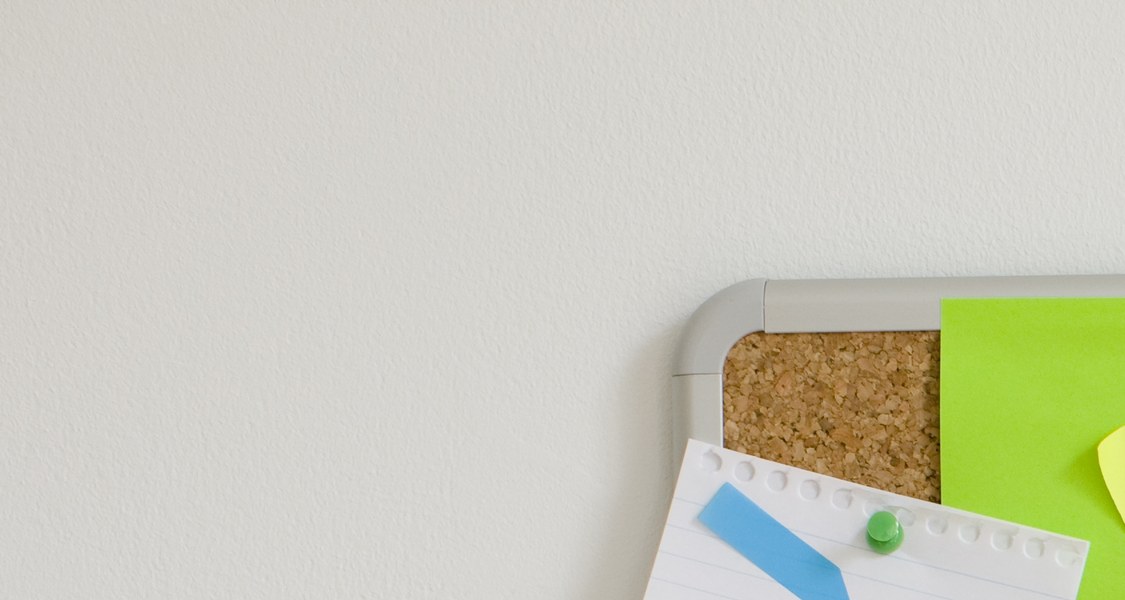 Auf dem Bild ist eine braune Korkpinnwand mit zahlreichen sich teilweise überlappenden Post-It Klebezetteln in verschiedenen Farben zu sehen. Das mittlere Post-it trägt die Aufschrift "Make things happen", englisch für "Mache Dinge geschehen" oder "Sorge dafür, dass Dinge passieren".