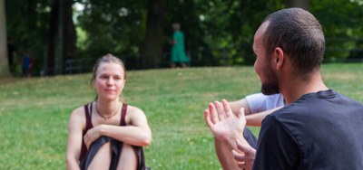 Eine Person erklärt etwas mit unterstützenden Gesten, während eine andere Person im Hintergrund zuhört und leicht lächelt.