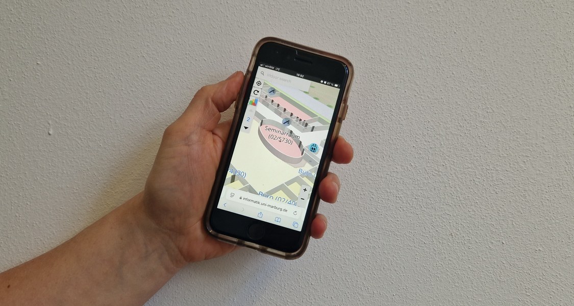 A hand holds a smartphone on which the MINKA application shows a seminar room