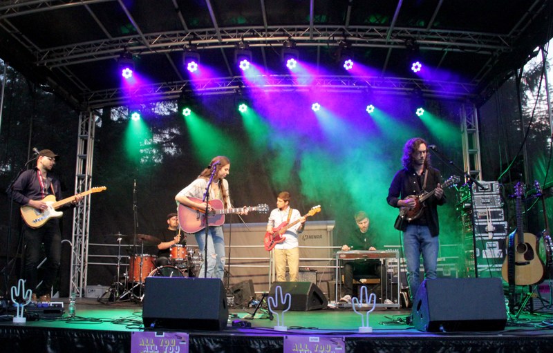 A six-member band is performing on stage at the university summer festival.
