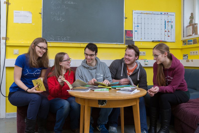 Five students sitting in a student council room, laughing together while looking at various brochures.